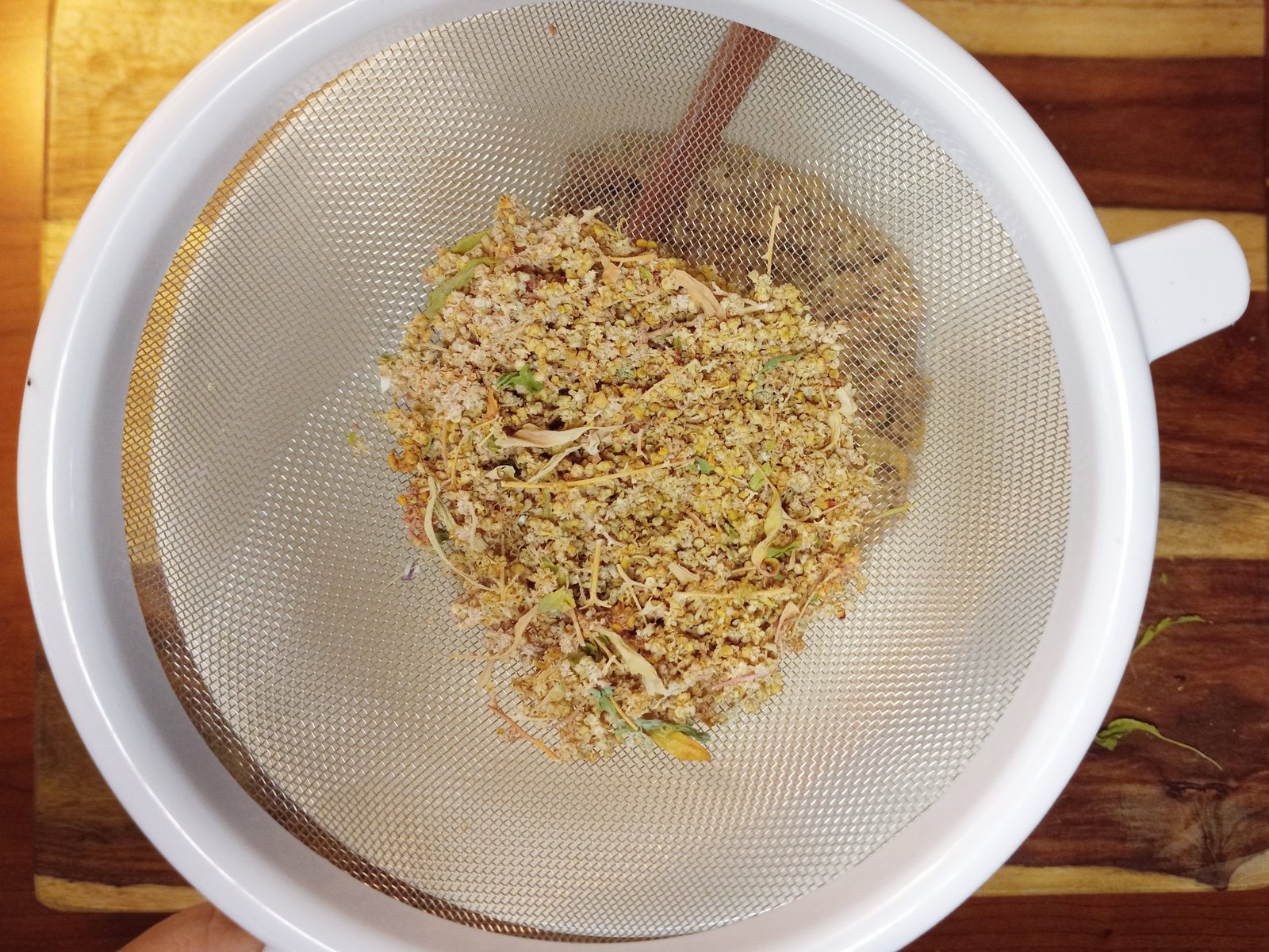 mesh strainer with plant debris and quinoa seeds